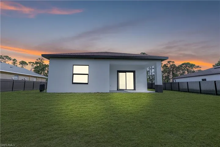 Back of property at dusk with a fenced backyard and stucco siding