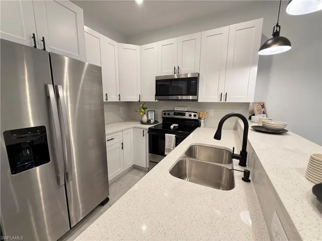 Kitchen featuring stainless steel appliances, light stone countertops, white cabinetry, and pendant lighting