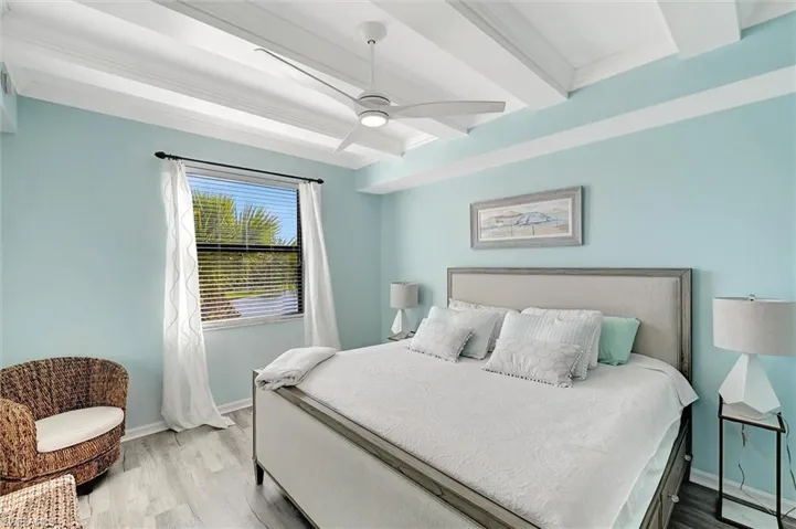 Bedroom featuring beamed ceiling, wood finished floors, and a ceiling fan
