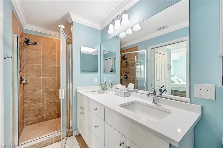 Full bath featuring double vanity, a shower stall, ornamental molding, and ensuite bathroom