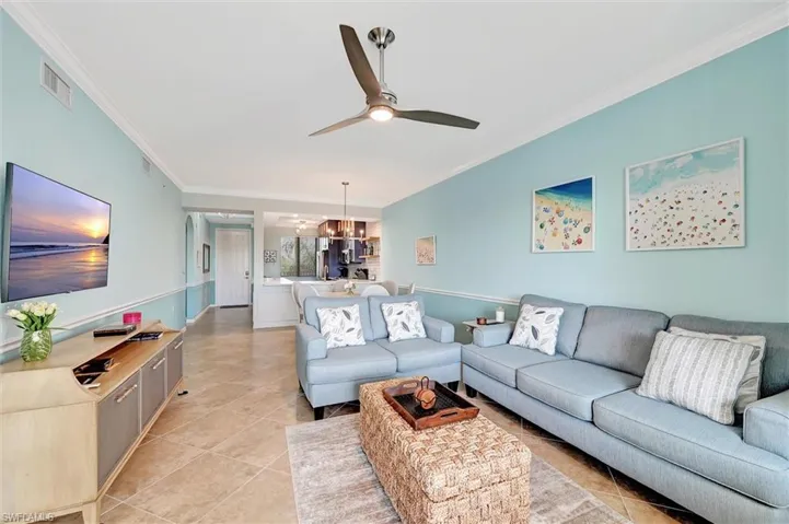 Living area with ornamental molding, a ceiling fan, light tile patterned floors, and a chandelier