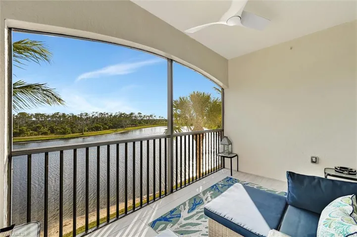 Balcony with a sunroom, a water view, ceiling fan, and view of wooded area