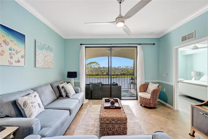 Living room featuring a water view, ornamental molding, ceiling fan, and tile patterned floors