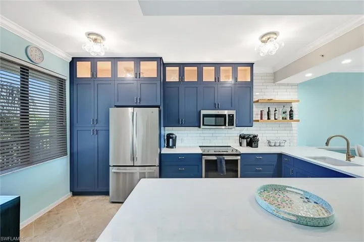 Kitchen with blue cabinetry, crown molding, appliances with stainless steel finishes, backsplash, and glass insert cabinets