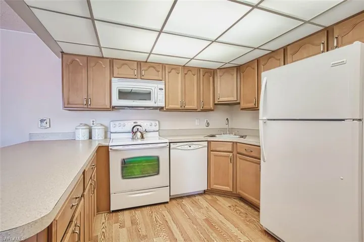 Kitchen with white appliances, light laminate floors, light countertops, and a drop ceiling