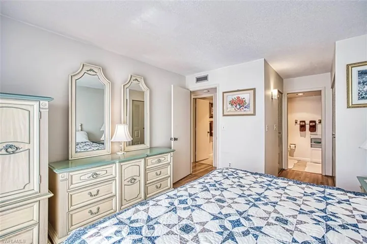 Bedroom with a textured ceiling, light laminate floors, and connected bathroom