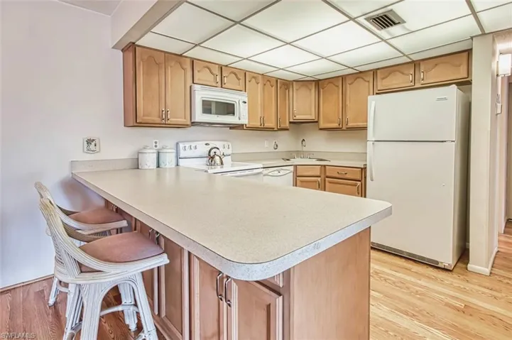 Kitchen featuring white appliances, light countertops, light laminate flooring, a peninsula, and a kitchen breakfast bar
