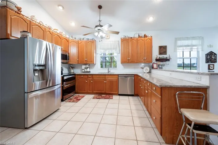 Kitchen with stainless steel appliances, vaulted ceiling, a breakfast bar, kitchen peninsula, and light stone countertops