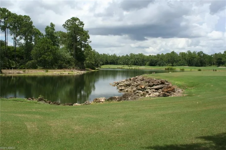 Expansive green space featuring a large body of water, mature trees, and a distant golf course
