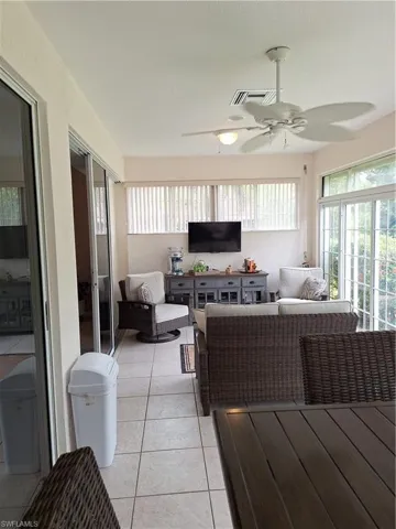 Screened porch featuring tiled flooring, multiple ceiling fans with integrated lighting, a full wall of windows with vertical blinds, and expansive sliding glass doors