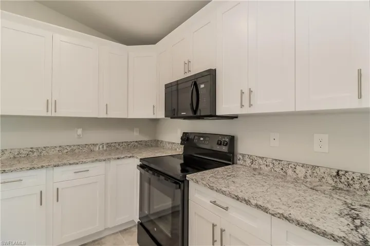 Kitchen with white cabinets, black appliances, light stone countertops, and lofted ceiling