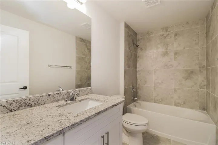 Full bathroom featuring tiled shower / bath combo, toilet, oversized vanity, and tile floors