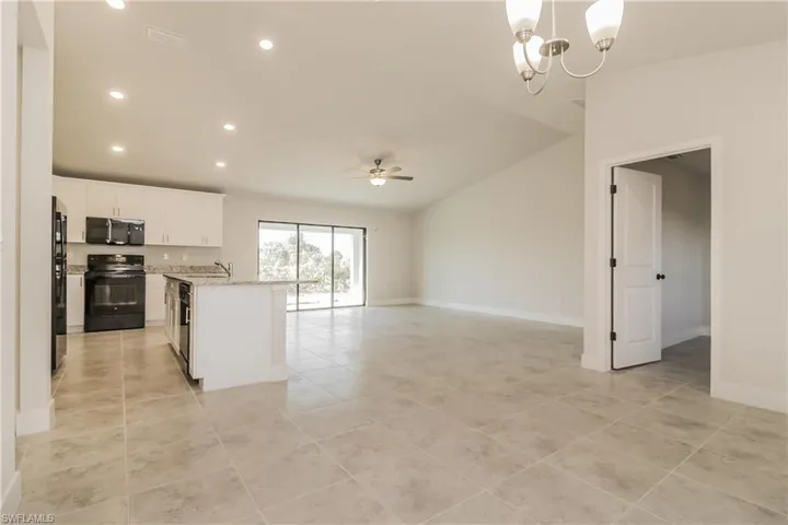 Kitchen featuring ceiling fan with notable chandelier, black appliances, a kitchen island with sink, white cabinets, and light tile floors