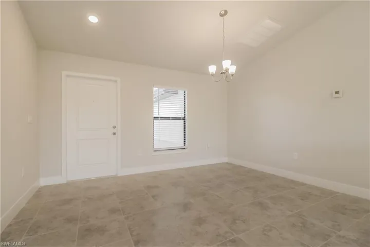 Empty room featuring vaulted ceiling, light tile flooring, and a chandelier