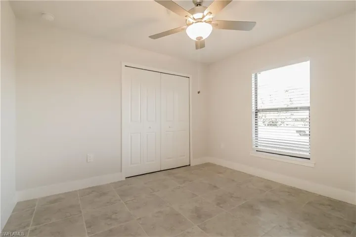 Unfurnished bedroom featuring a closet, light tile flooring, and ceiling fan