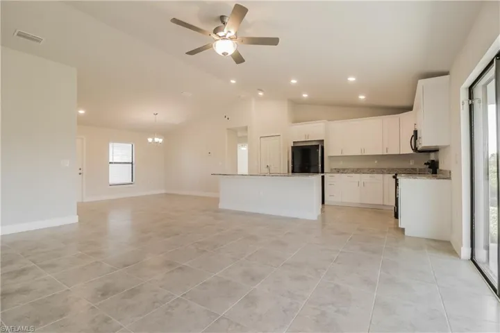 Kitchen with a center island with sink, light tile flooring, ceiling fan with notable chandelier, white cabinets, and refrigerator