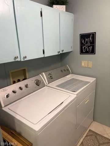 Clothes washing area with cabinets, washing machine and dryer, and light tile patterned floors