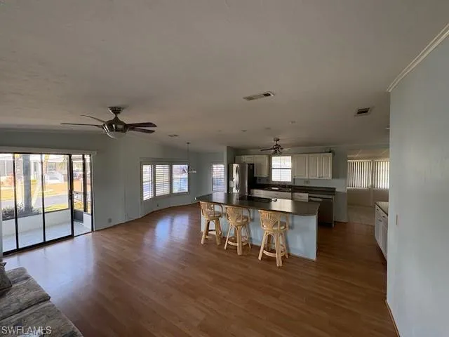 Kitchen with dark countertops, a ceiling fan, a kitchen island, stainless steel refrigerator with ice dispenser, and a breakfast bar