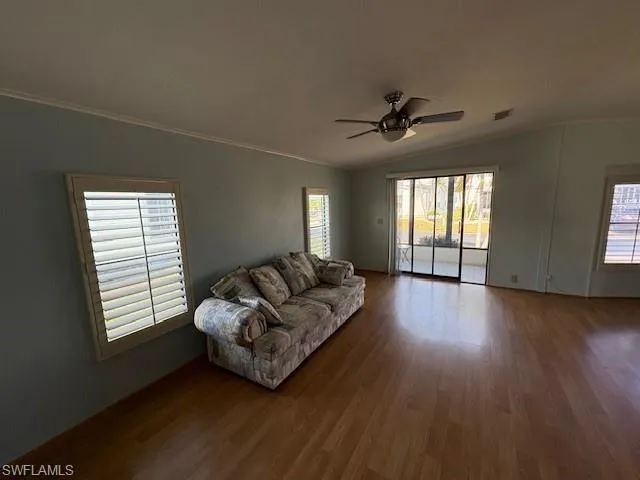 Living area with crown molding, lofted ceiling, visible vents, ceiling fan, and wood finished floors