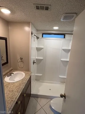 Full bath with vanity, a textured ceiling, a stall shower, and visible vents
