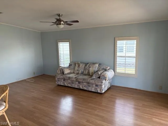 Living room with visible vents, ceiling fan, wood finished floors, and ornamental molding
