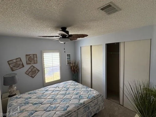 Carpeted guest bedroom with multiple closets, a textured ceiling, visible vents, and ceiling fan