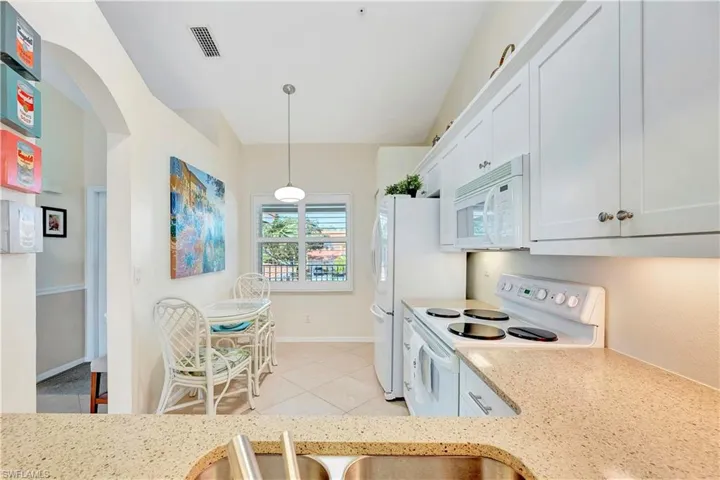 Kitchen with white cabinets, pendant lighting, light stone counters, and white appliances