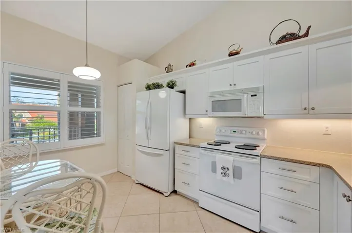 Kitchen with white appliances, light tile patterned floors, decorative light fixtures, white cabinets, and lofted ceiling