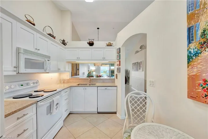 Kitchen featuring white appliances, vaulted ceiling, sink, white cabinetry, and light tile patterned flooring