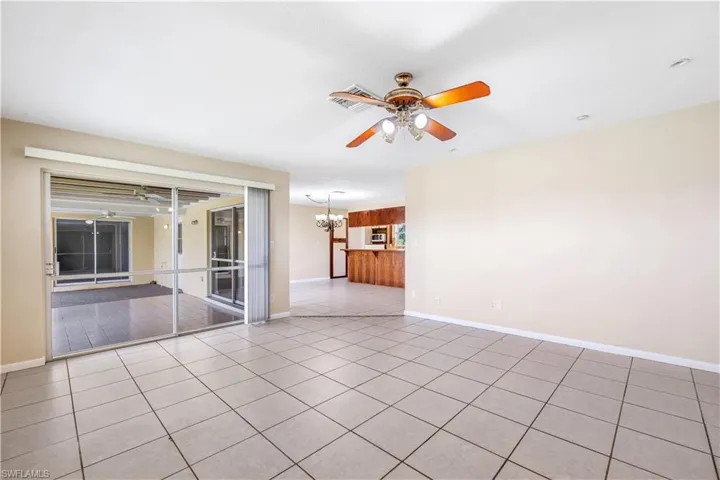 Tiled empty room featuring ceiling fan with notable chandelier