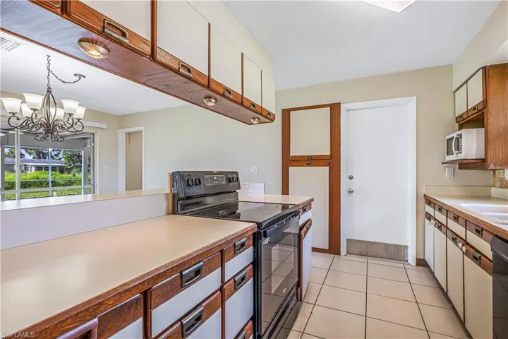 Kitchen featuring black electric range oven, a notable chandelier, dishwasher, light tile patterned floors, and decorative light fixtures