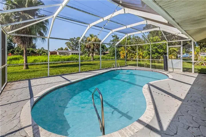 View of pool with glass enclosure, a patio, and a lawn