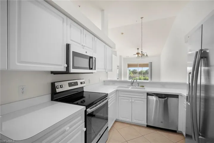 Kitchen with stainless steel appliances, light countertops, white cabinets, vaulted ceiling, and suspended lighting