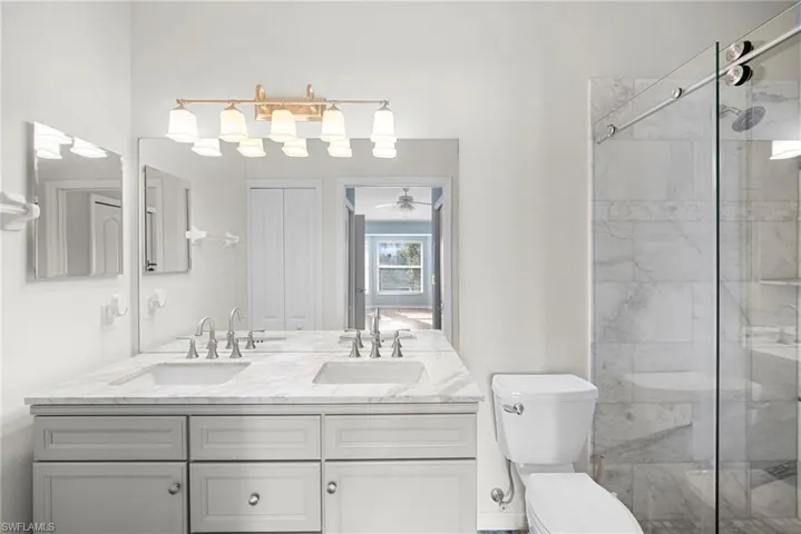 Bathroom with double vanity, a marble finish shower, ceiling fan, and a closet