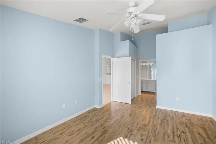Unfurnished bedroom featuring light wood-style flooring, a ceiling fan, a high ceiling, and ensuite bathroom