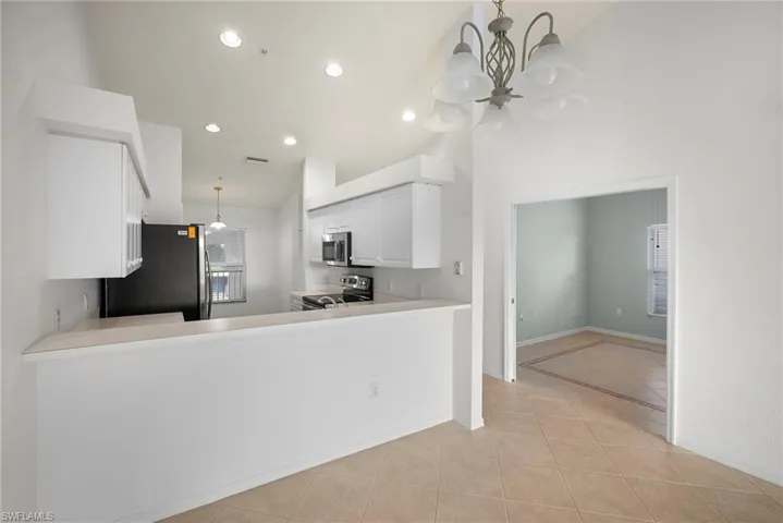 Kitchen featuring light countertops, white cabinetry, stainless steel appliances, suspended lighting, and vaulted ceiling