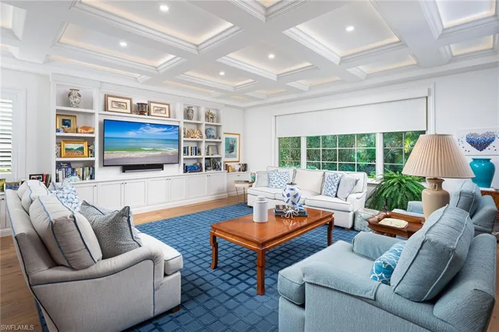 Living area featuring wood finished floors, coffered ceiling, beamed ceiling, built in shelves, and crown molding
