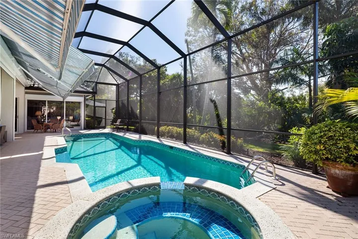 View of swimming pool featuring a pool with connected hot tub, a patio area, a sunroom, glass enclosure, and outdoor dining space