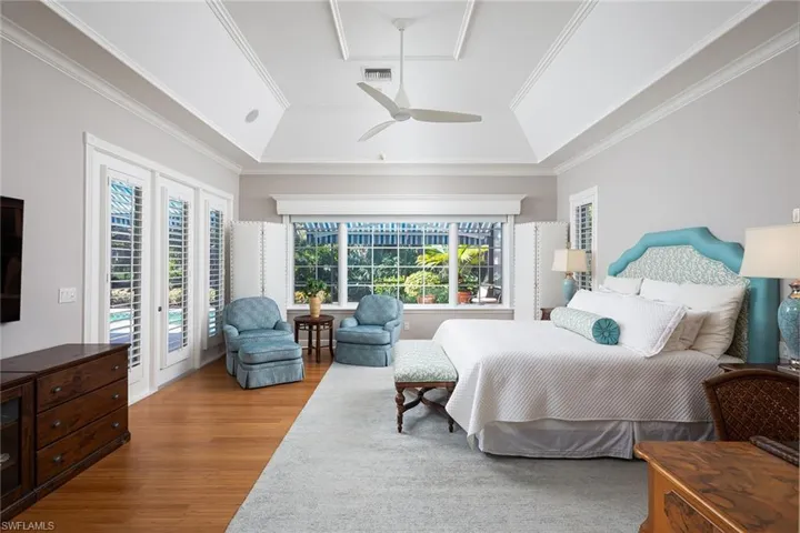Bedroom with access to outside, wood finished floors, ceiling fan, a tray ceiling, and crown molding