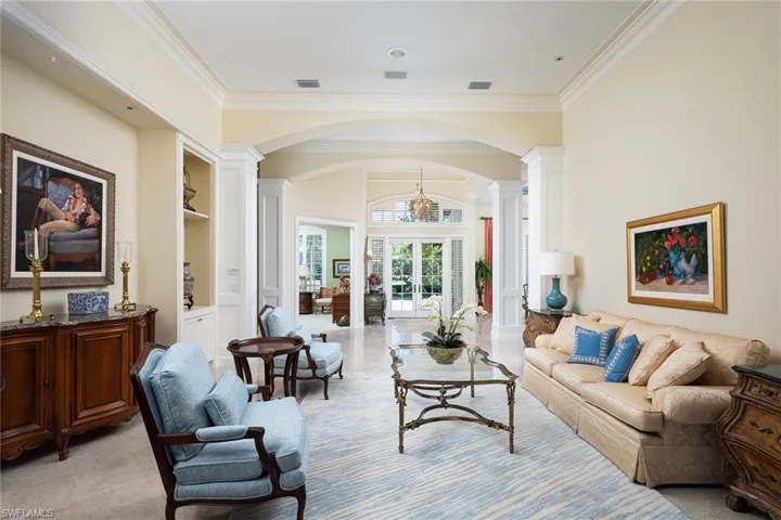 Living area with arched walkways, french doors, ornate columns, crown molding, and built in shelves