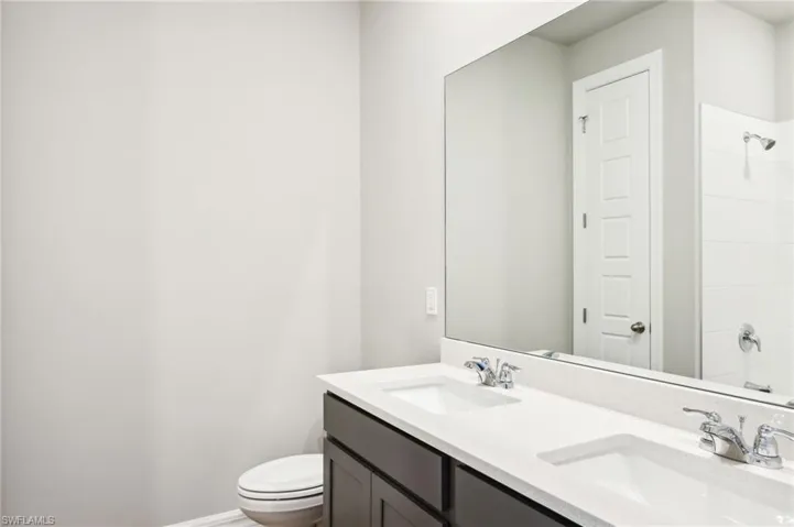 Full bath with double vanity, toilet, and baseboards