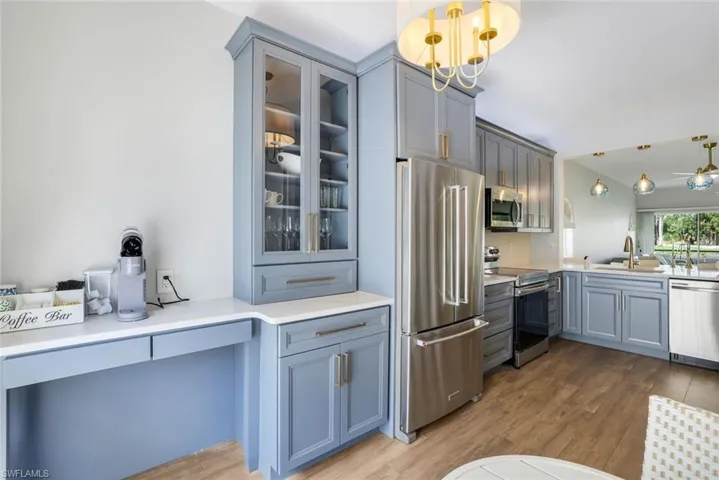 Kitchen featuring gray cabinets, a sink, appliances with stainless steel finishes, glass insert cabinets, and wood finished floors