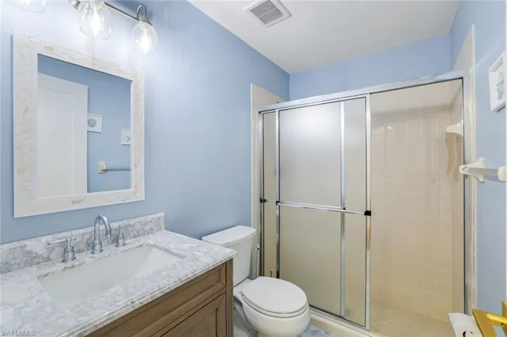 Full bathroom with a shower stall, visible vents, toilet, and vanity