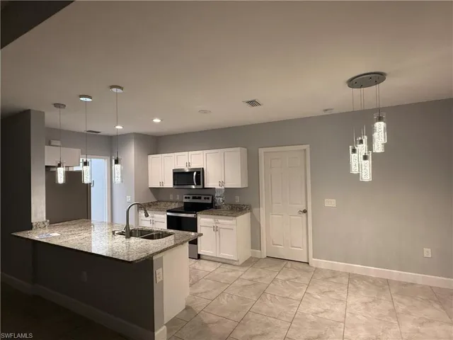 Kitchen featuring white cabinets, decorative light fixtures, kitchen peninsula, and appliances with stainless steel finishes
