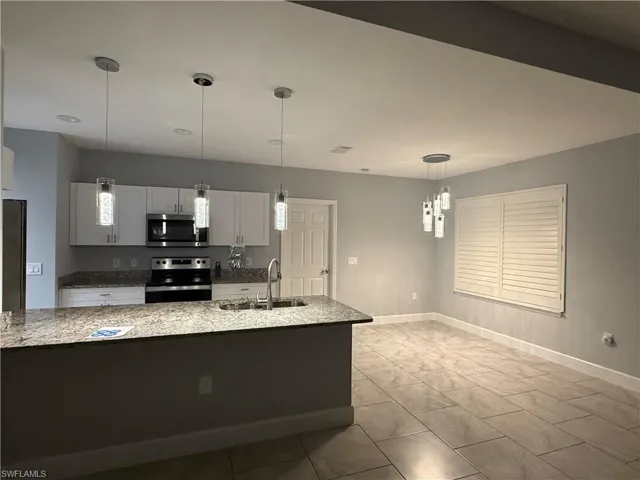 Kitchen with sink, light stone counters, decorative light fixtures, white cabinets, and appliances with stainless steel finishes