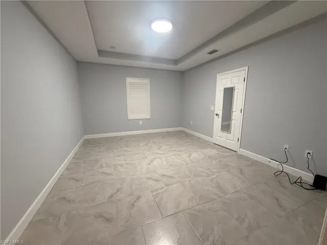 Spare room with a tray ceiling, marble finish floor, visible vents, and baseboards