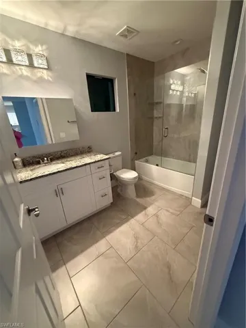 Full bathroom featuring marble finish floor, visible vents, toilet, enclosed tub / shower combo, and vanity