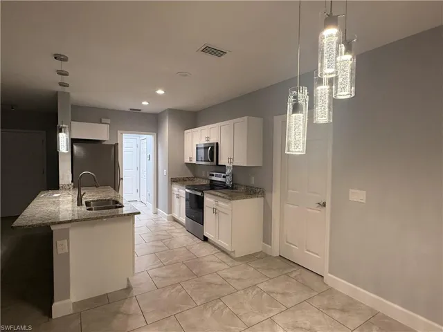 Kitchen with white cabinets, decorative light fixtures, sink, and stainless steel appliances