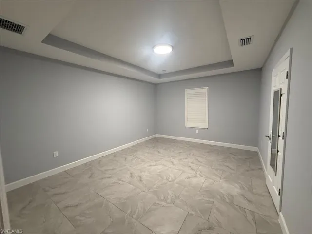 Spare room featuring marble finish floor, a tray ceiling, visible vents, and baseboards