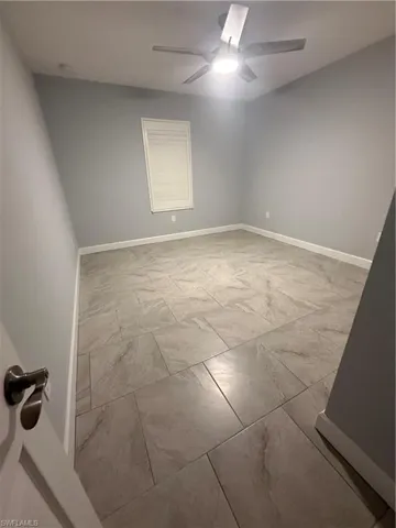 Empty room with marble finish floor, baseboards, and a ceiling fan